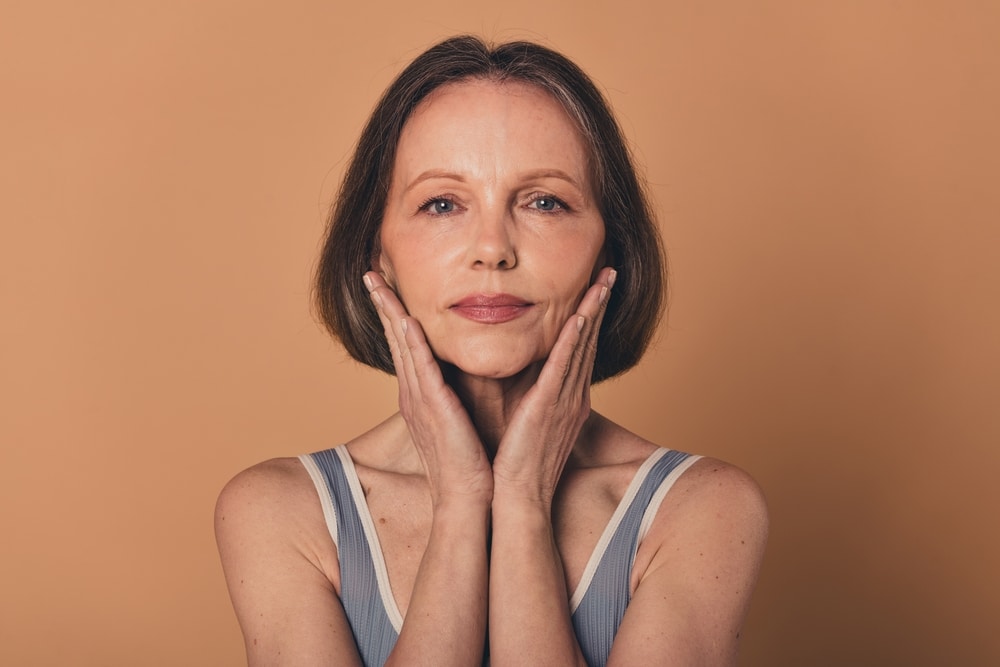 A beautiful older woman holding her face in her hands after recovering from facelift surgery to refresh her look. A beautiful older woman holding her face in her hands after recovering from facelift surgery to refresh her look.