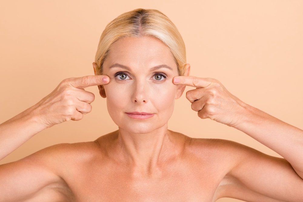 Middle-aged woman looking at the camera and pointing to her eyes to emphasize her blepharoplasty. Middle-aged woman looking at the camera and pointing to her eyes to emphasize her blepharoplasty.